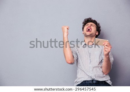 Happy man holding smartphone and celebrating his success over gray background