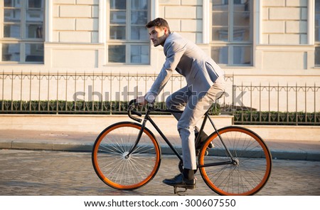 Handsome businessman riding bicycle to work on urban street in morning