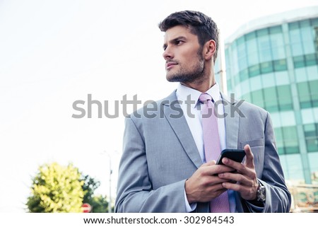Bsinessman using smartphone and looking away outdoors