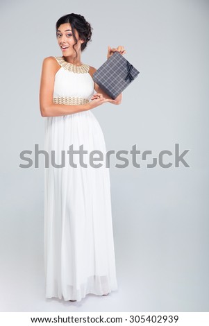 Full length portrait of a beautiful woman in dress holding gift box on gray background. Looking at camera