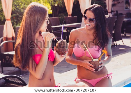 Portrait of a two girls in bikini drinking cocktails and gossip outdoors