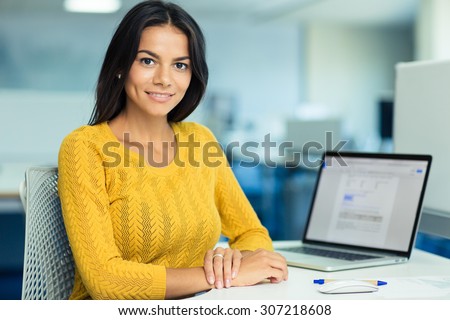Portrait of a happy casual businesswoman in sweater sitting at her workplace in office
