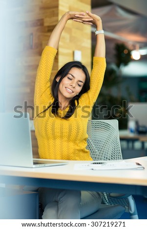 Portrait of a happy businesswoman sitting at the table and stretching hands in office