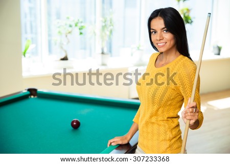 Happy young woman playing billiards indoors