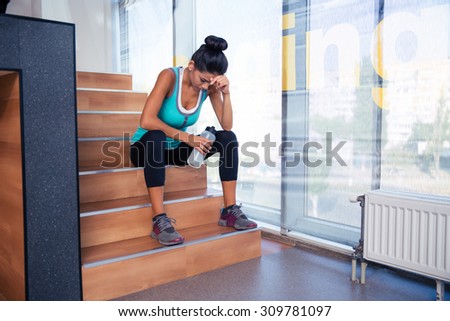 Tired woman sitting on the stairs with bottle of water in gym