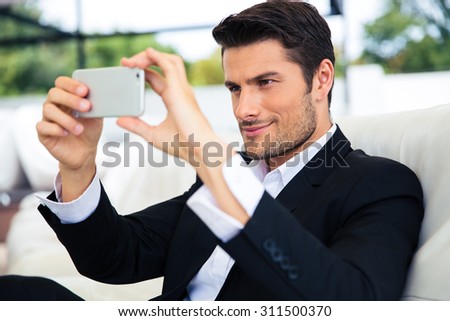 Confident businessman making selfie photo on smartphone in restaurant