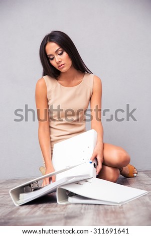 Tired businesswoman sitting on the floor with folders on gray background
