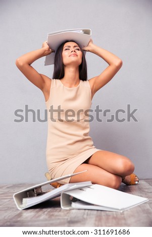 Tired businesswoman sitting on the floor with folders on gray background
