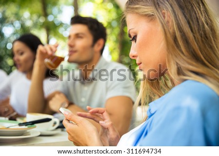 Portrait of a beautiful woman using smartphone while sitting in outdoor restaurant with friends