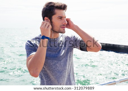 Sports man standing with headphones near sea outdoors and looking away