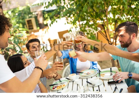 Group of a friends making toast around table at dinner party in outdoor restaurant