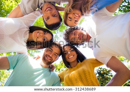 Group of smiling friends hugging together at the park in a circle
