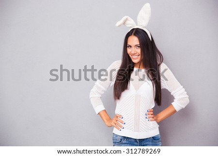 Portrait of a cheerful woman in bunny ears standing on gray background