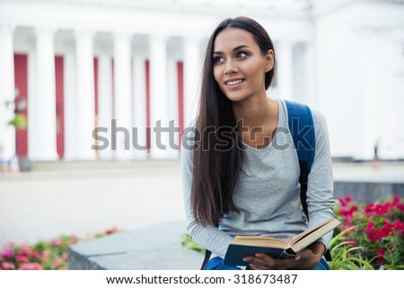 Portrait of a smiling female student holding book and looking away outdoors