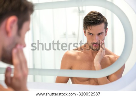 Portrait of a young man looking at his reflection in the mirror in bathroom
