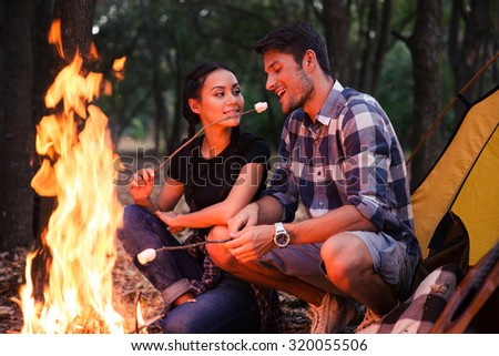 Happy couple fried sausages on bonfire in the forest