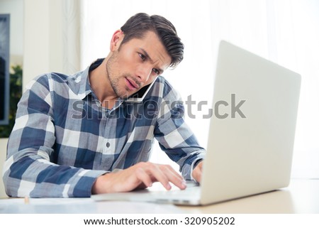 Portrait of a man paying his bills with laptop while talking on phone at home