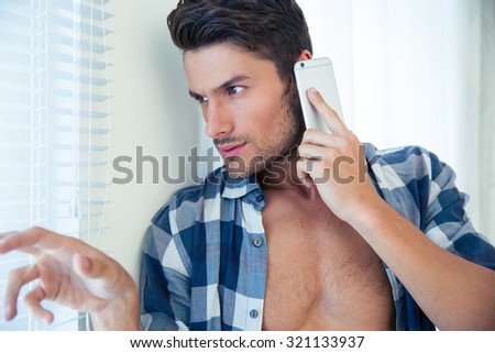 Portrait of a young man talking on the phone and looking in window at home