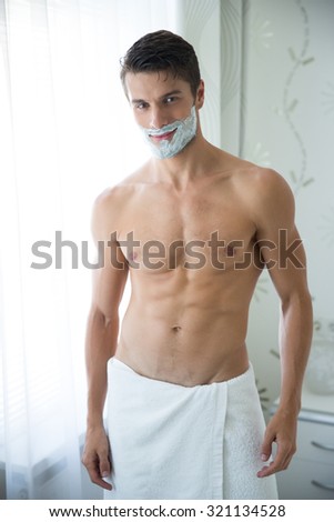 Portrait of a handsome man with foam on face standing in bathroom