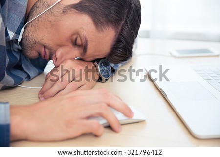 Portrait of a young man with headphones sleeping at the table with laptop at home