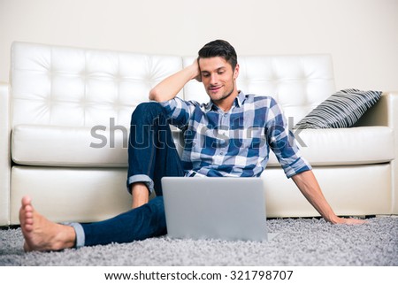 Portrait of a happy man sitting on the floor with laptop at home
