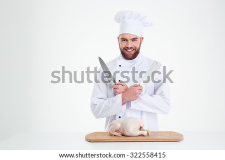 Portrait of a happy male chef cook standing with knifes and chicken on the table isolated on a white background