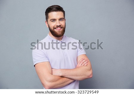 Portrait of a happy casual man standing with arms folded over gray background and looking at camera