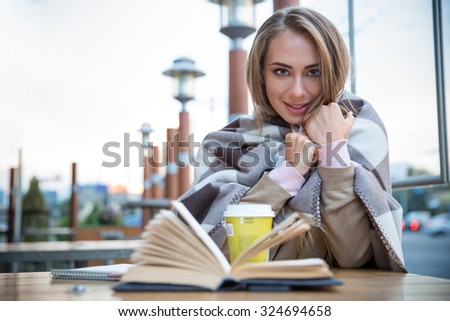 Portrait of a happy female student sitting with book and coffee in cafe