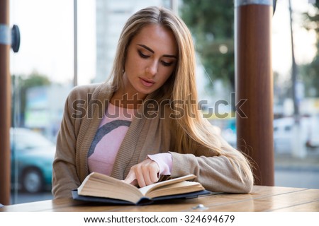 Portrait of a charming girl reading book in cafe
