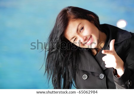 Young happy brunette woman on the beach winking and pointing at you