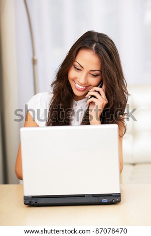 Portrait of pretty happy young woman on phone with laptop sitting at the table