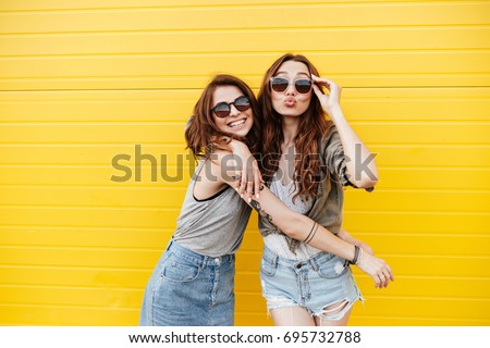 Image of two young happy women friends standing over yellow wall. Looking at camera blowing kisses. ストックフォト © 