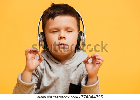 Photo of little concentrated boy child sitting on floor isolated over yellow background with eyes closed listening music with headphones. ストックフォト © 