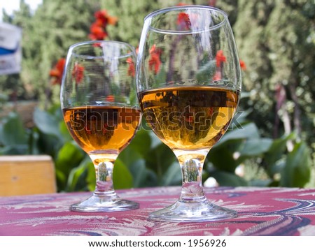 Two glasses with a wine on a little table of cafe. On a background red flowers and greens.