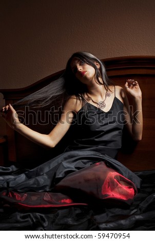 Beautiful young woman in black and red dress sitting on bed