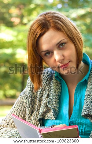 Red-haired woman reading a book in early autumnal park