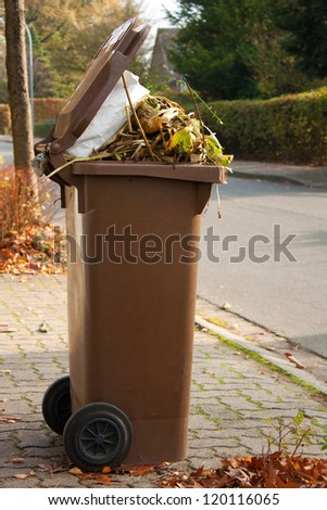 Overflowing brown garbage bin or can full with dead autumn leaves and plants