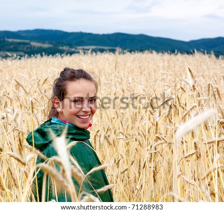 Young woman with a rain coat walking through wheat field