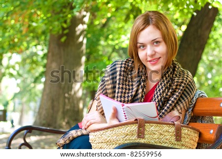Beautiful red-haired woman reading in the park and smilling at camera