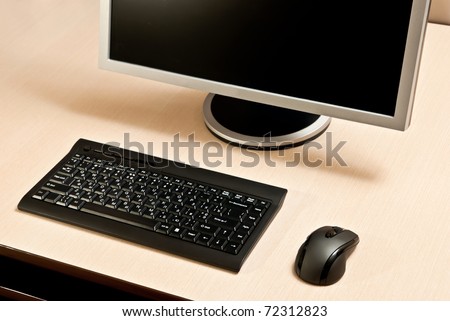 Black keyboard, mouse and monitor on a wood desk.