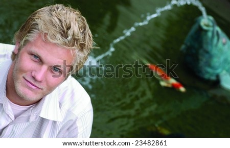 Interesting angle of good looking blond guy in front of koi pond.