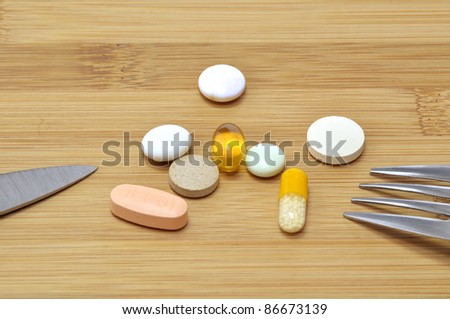 Capsule and pills on wooden breakfast board with knife and fork