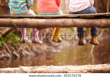Close Up Of Children's Feet Dangling From Wooden Bridge