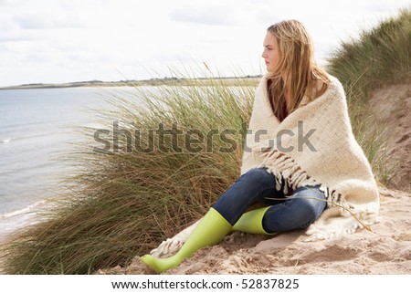 Young Woman Standing In Sand Dunes Wrapped In Blanket