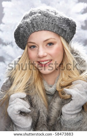 Fashionable Teenage Girl Wearing Cap And Fur Coat In Studio In Front Of Christmas Tree