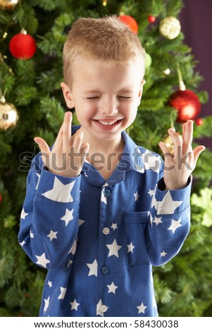 Young Boy Crossing Fingers In Front Of Christmas Tree