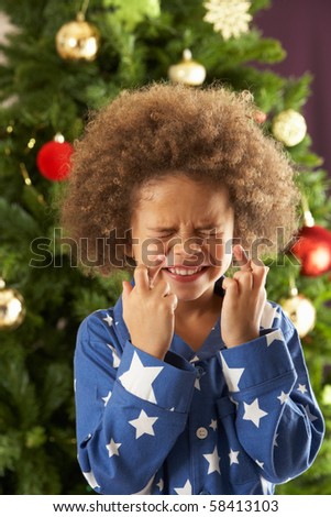 Young Boy Crossing Fingers In Front Of Christmas Tree
