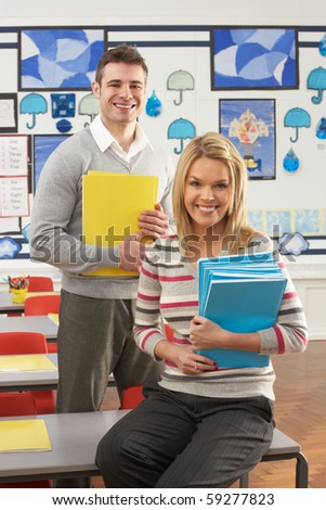 Portrait Of Male And Female Teacher Sitting At Desk In Classroom