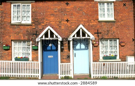 Side by side, pastel blue doors making a nice contrast, a pair of Victorian brick built terraced cottages with white picket fencing