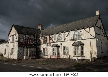 A rather dramatic image of an abandoned roadside hotel in Devon England. Hotel crumbling into disrepair caught in a moment of bright sunshine on an otherwise dark and stormy day